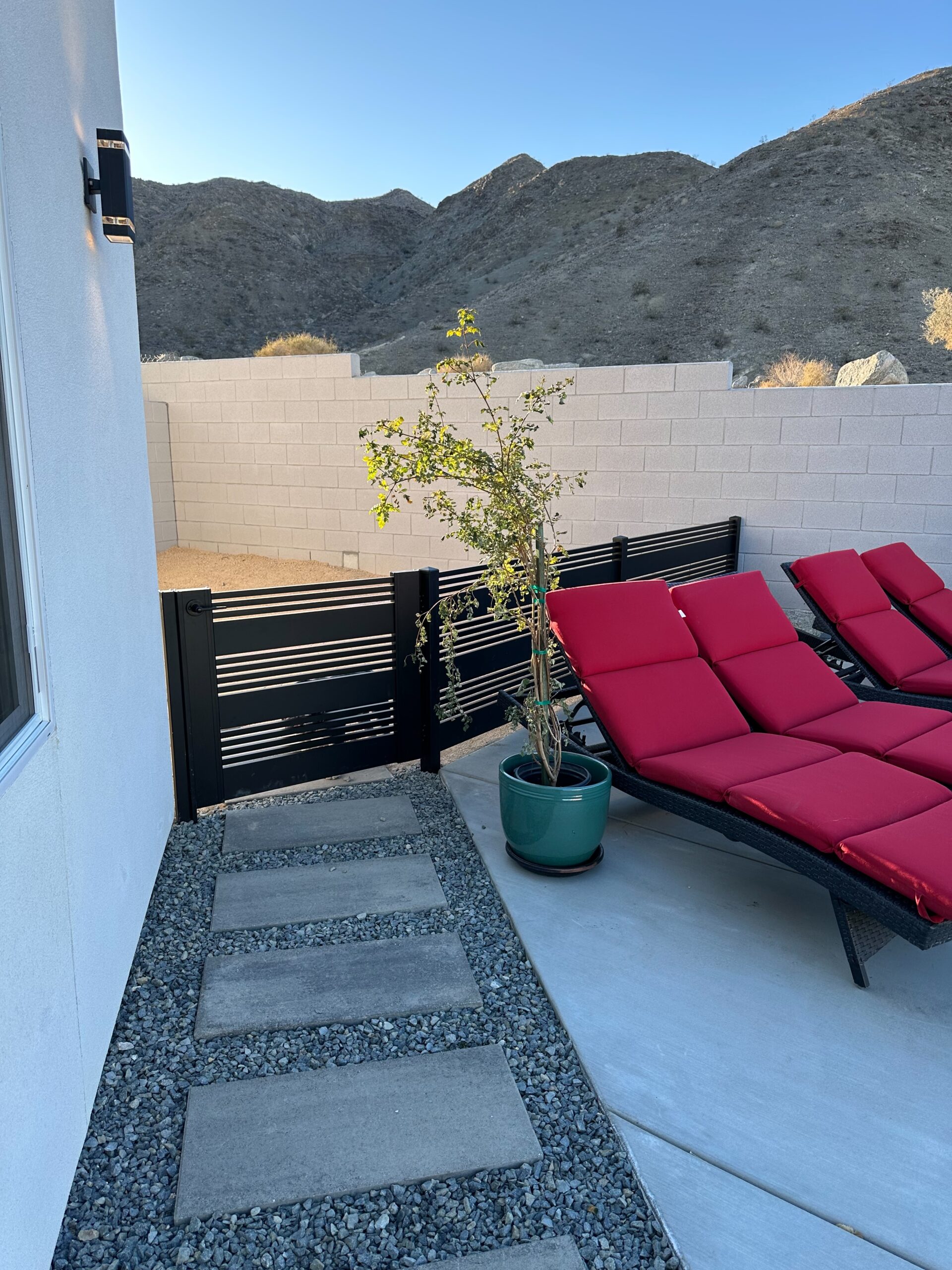 Matte black aluminum gate with slats near red lounge chairs in a desert setting.