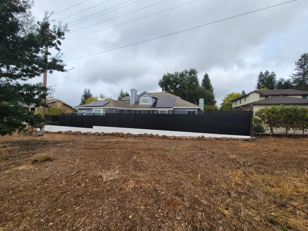 View across an open yard toward a black aluminum fence and neighboring houses.