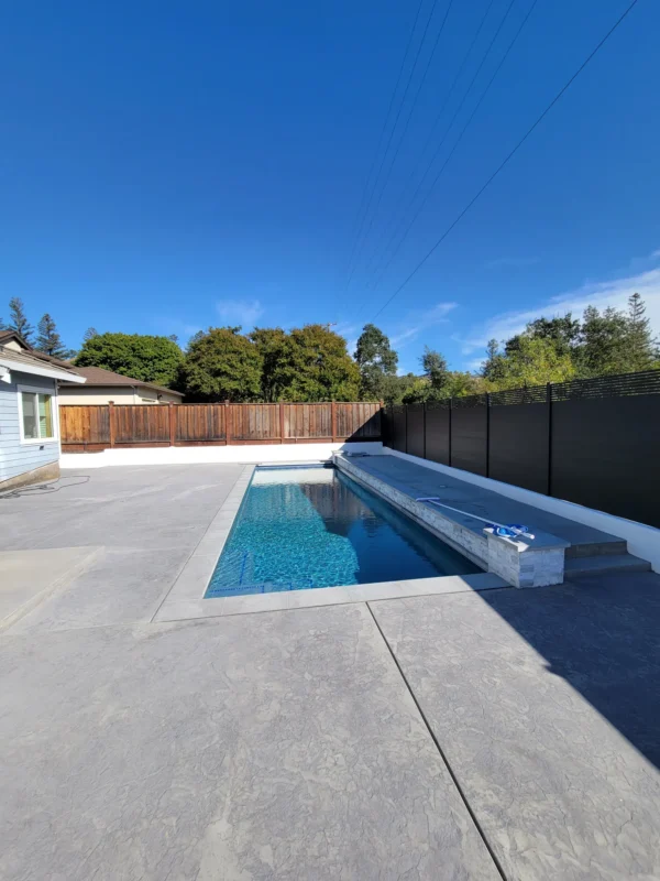 Backyard pool and patio with a completed black aluminum fence along the right side.