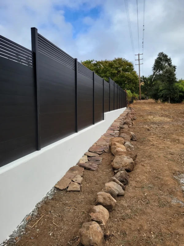 Black aluminum fence above a white concrete base along a dirt side yard.