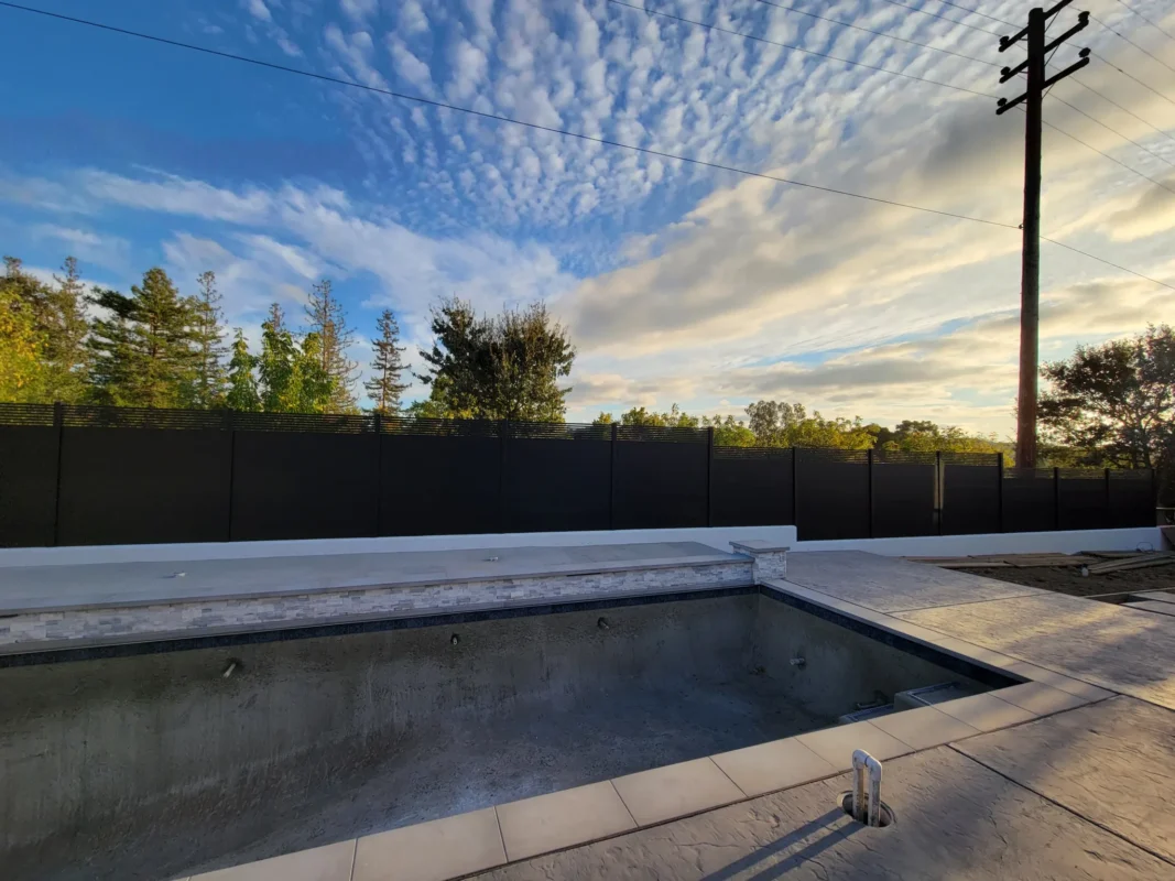 Black aluminum fence with solid lower slats and spaced upper slats beside a pool at sunset.
