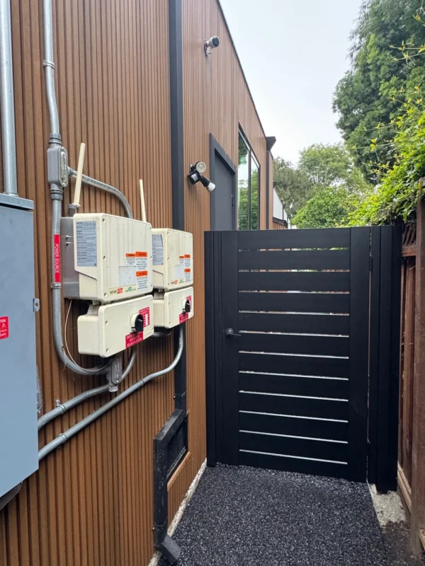 Black Los Angeles style pedestrian side gate with horizontal slats and handle, next to modern brown siding.