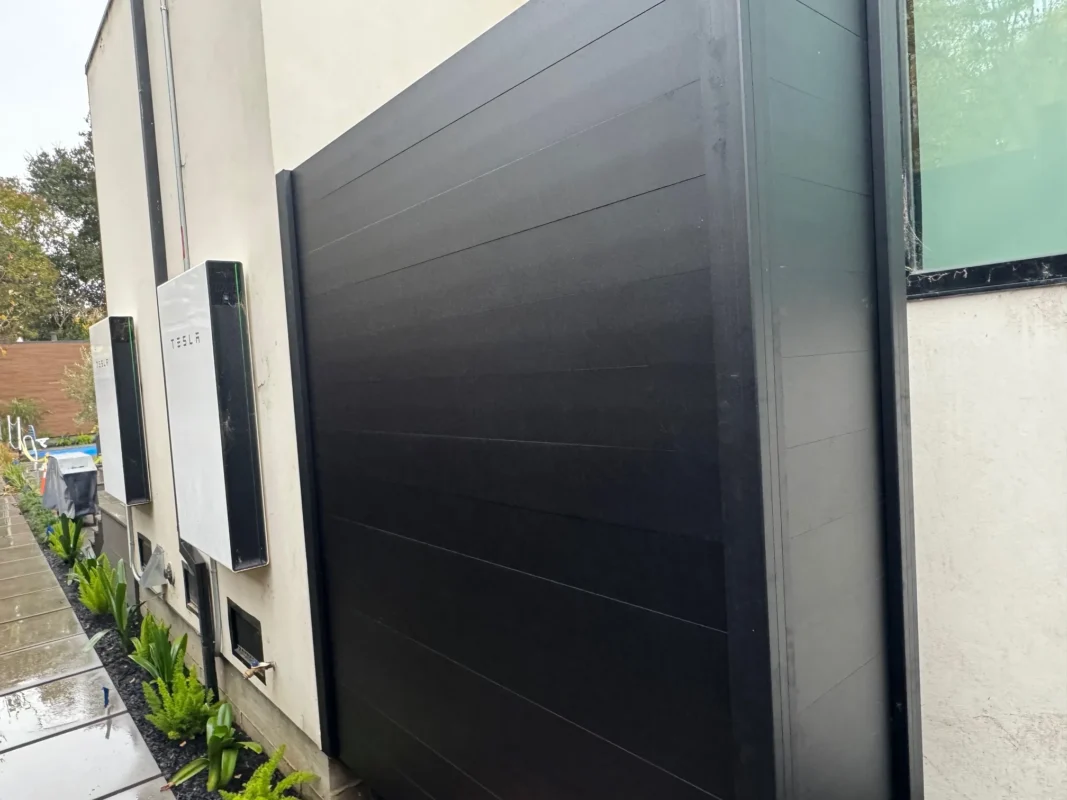 Black full privacy enclosure panels surrounding outdoor equipment with black gravel on the ground.