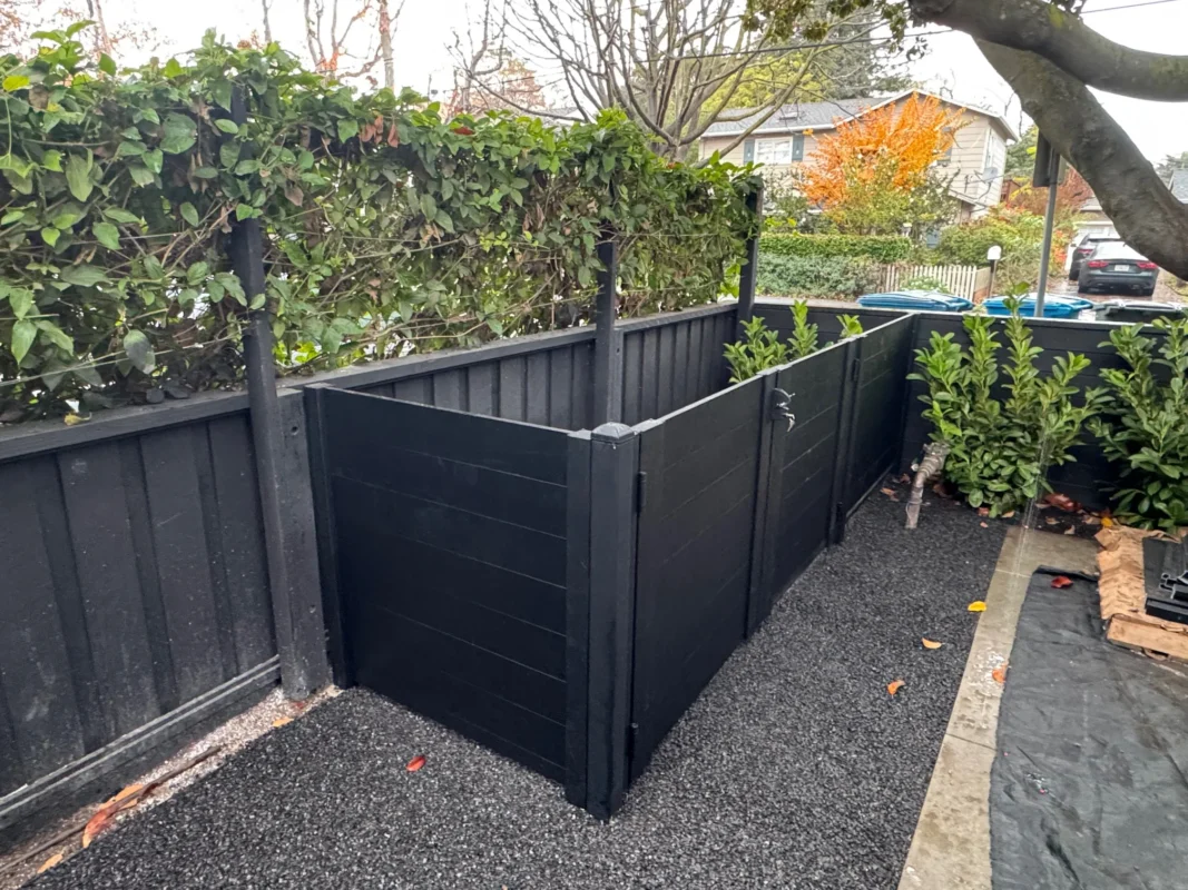 Black full privacy enclosure surrounding outdoor equipment with greenery above enclosure.