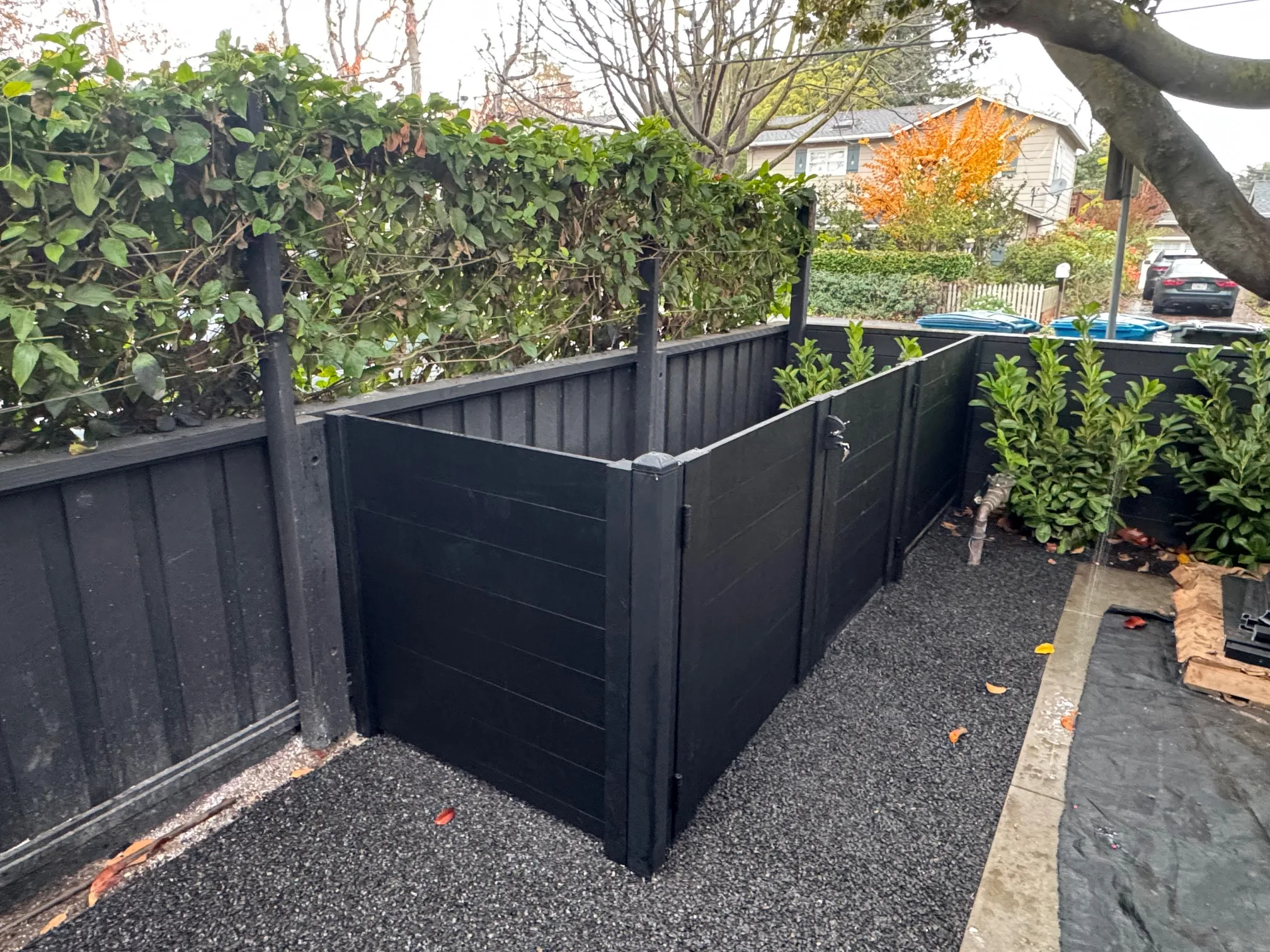 Black full privacy enclosure surrounding outdoor equipment with greenery above enclosure.