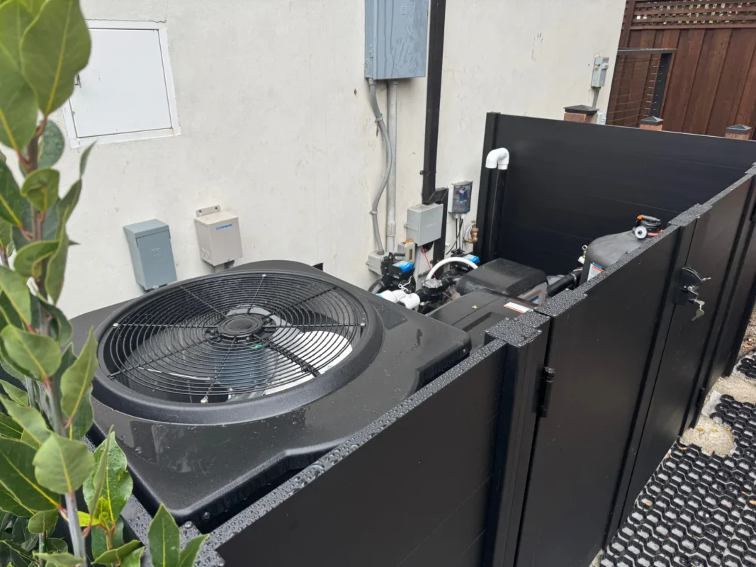 Black full privacy enclosure panels installed in landscaping area, enclosing outdoor mechanical equipment.