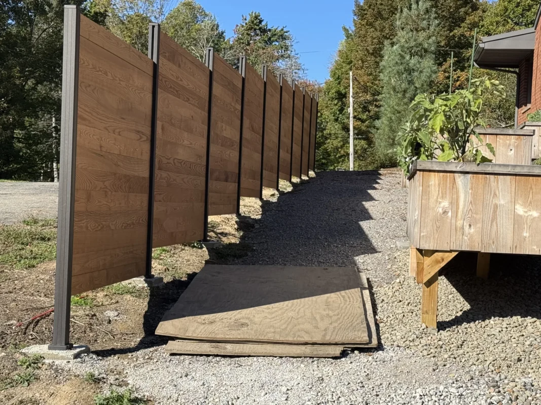 Fence panels featuring custom wood slats slid into dark aluminum posts along gravel driveway.
