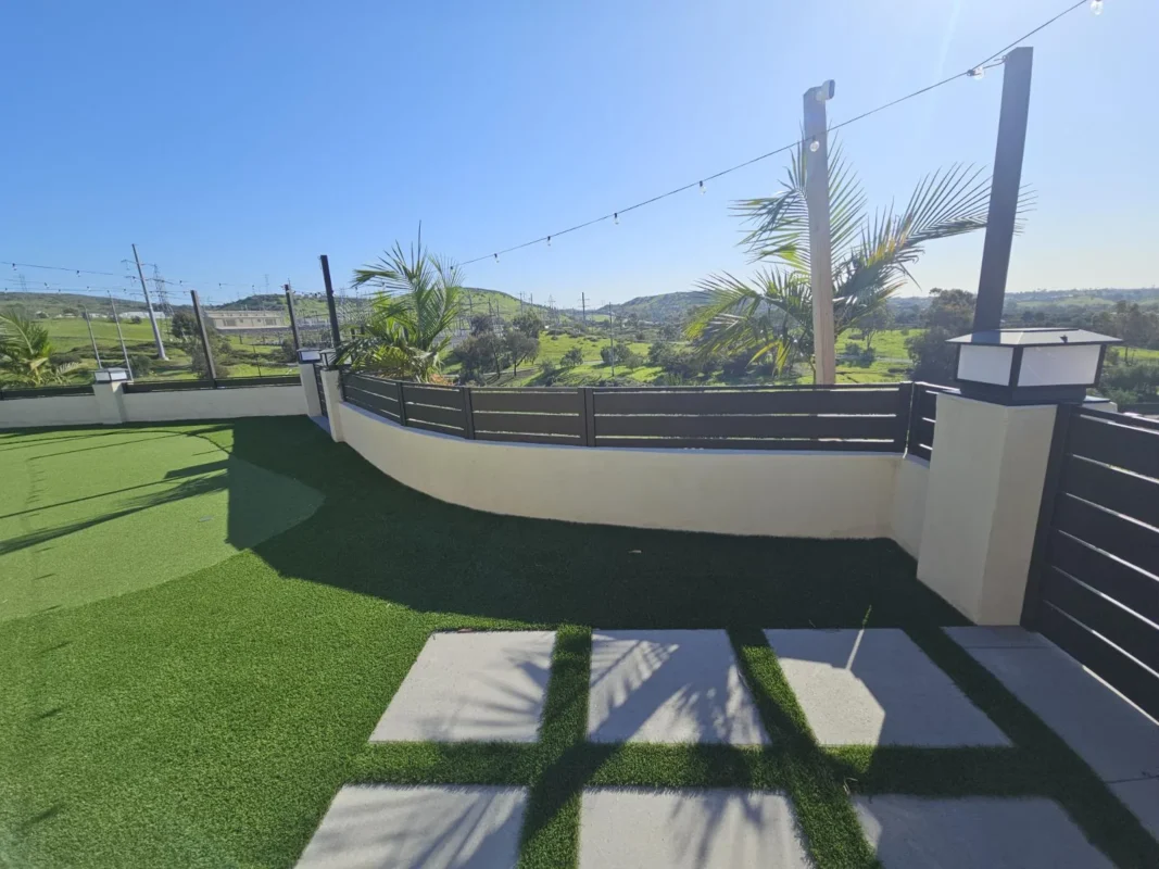 Black Miami style aluminum horizontal slat wall topper fences on low masonry walls enclosing a patio with artificial turf and square stepping stones