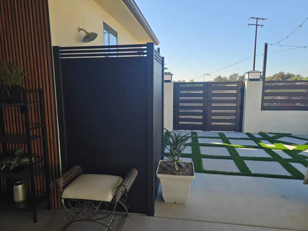 Black privacy aluminum panel near house entrance with double swing gate in background featuring horizontal slats and masonry posts